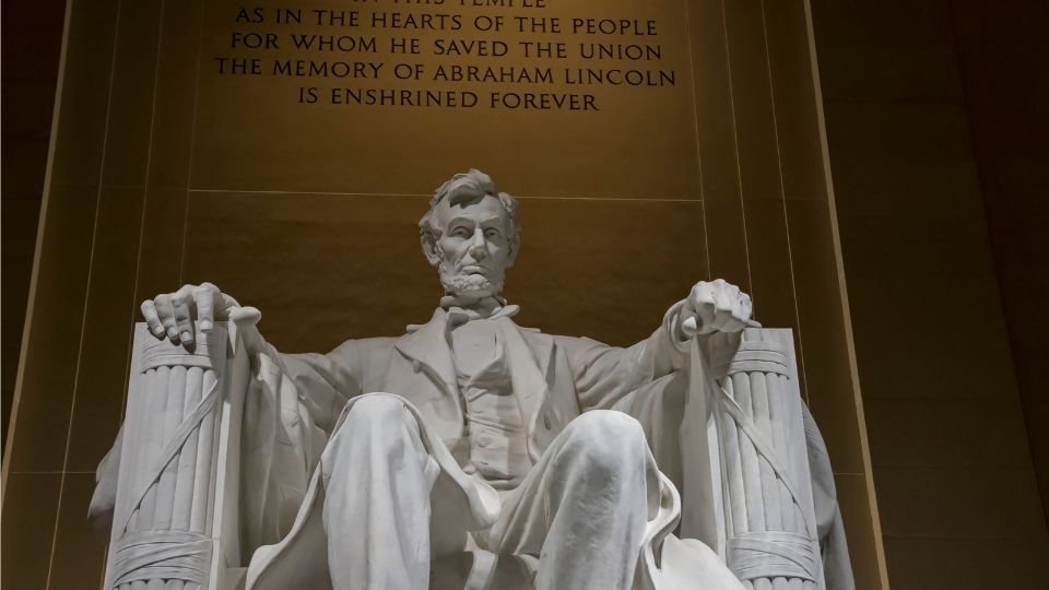 Abraham Lincoln szobra a Lincoln-emlékhelyen, háttérben feliratokkal.