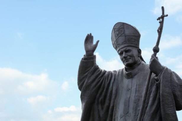 II. János Pál pápa szobra, amely integet a látogatóknak egy világos égen.