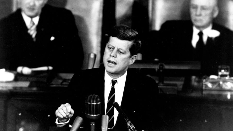 John F. Kennedy beszédet mond a kongresszus előtt, háttérben más politikai vezetők.