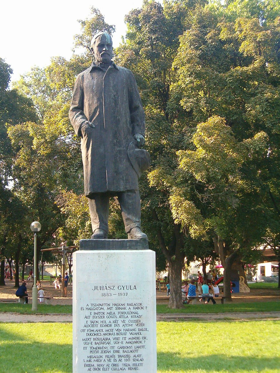 Juhász Gyula szobra egy parkban, zöld fákkal körülvéve.