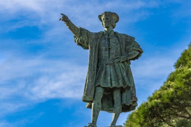 Kolumbusz Kristóf szobra, amely az égre mutat, háttérben kék ég és fák.