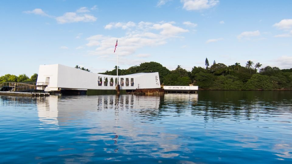 A Pearl Harbor-i USS Arizona emlékhely, amely a víz tükrében látható, zöld dombokkal körülvéve.