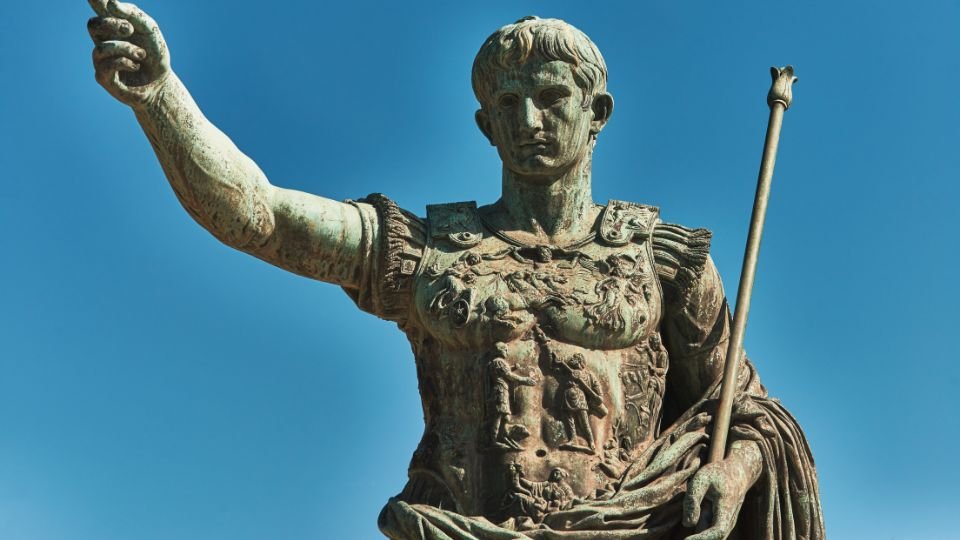 Római császár szobra, karját felemelve, hatalmat sugározva.