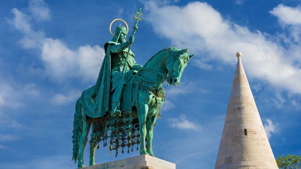 Szent István király bronzszobra, lóháton állva, háttérben kék ég és fehér felhők.