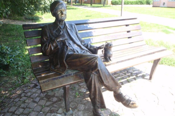 Bronz szobor egy férfiról, aki ül egy padon, mellette egy macska.
