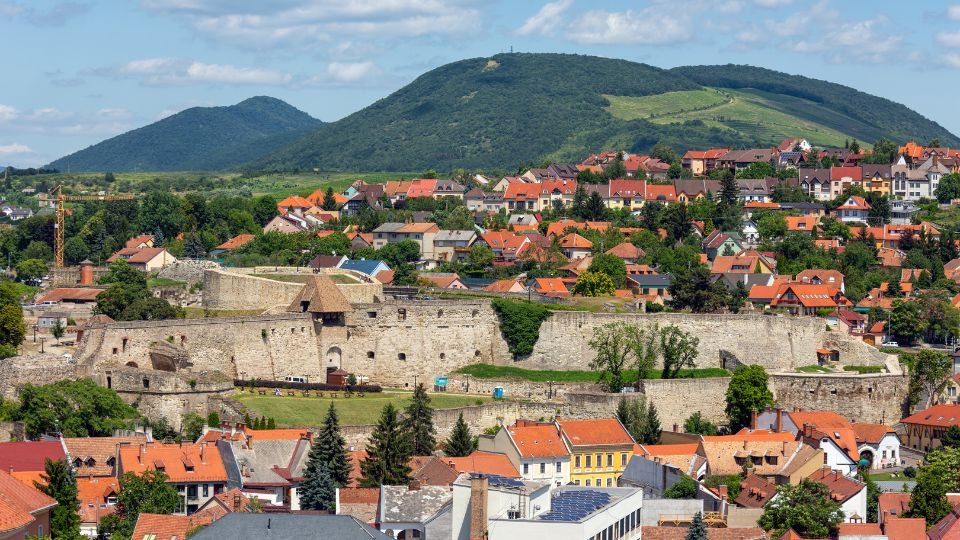 Az egri vár és a környező városrész panorámája, zöld dombokkal a háttérben.