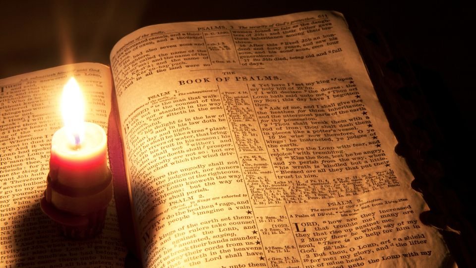 Egy gyertya világít egy nyitott Biblián, amely a Zsoltárok könyvét mutatja.