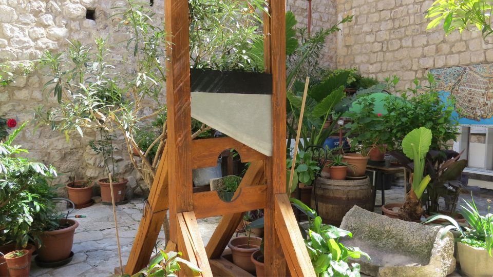 Egy guillotine áll egy zöld növényekkel teli udvarban, kövek között.