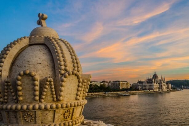 A budapesti Parlament és a Duna látképe naplementében, a koronás díszítéssel előtérben.