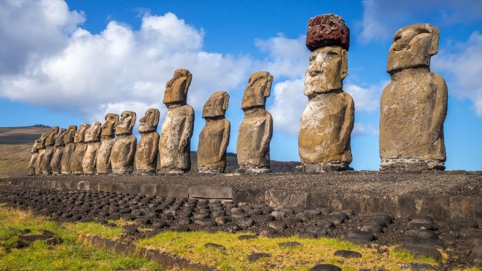 Húsvét-szigeti moai szobrok sorakoznak a tengerparton, zöld fűvel körülvéve.