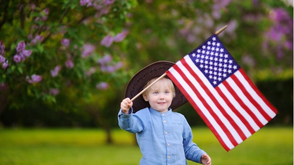Egy kisfiú amerikai zászlót lenget egy virágzó fa alatt.
