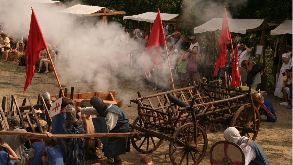 Középkori ostromjáték, füst és zászlók a háttérben.