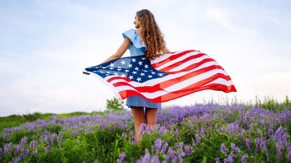 Egy fiatal nő az amerikai zászlót lengeti egy lila virágos mezőn, július 4-én.