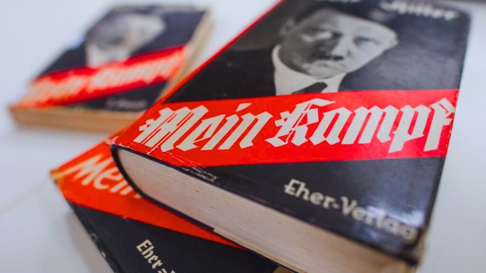Három példány Adolf Hitler Mein Kampf című könyvéből, fekete borítóval és piros felirattal.